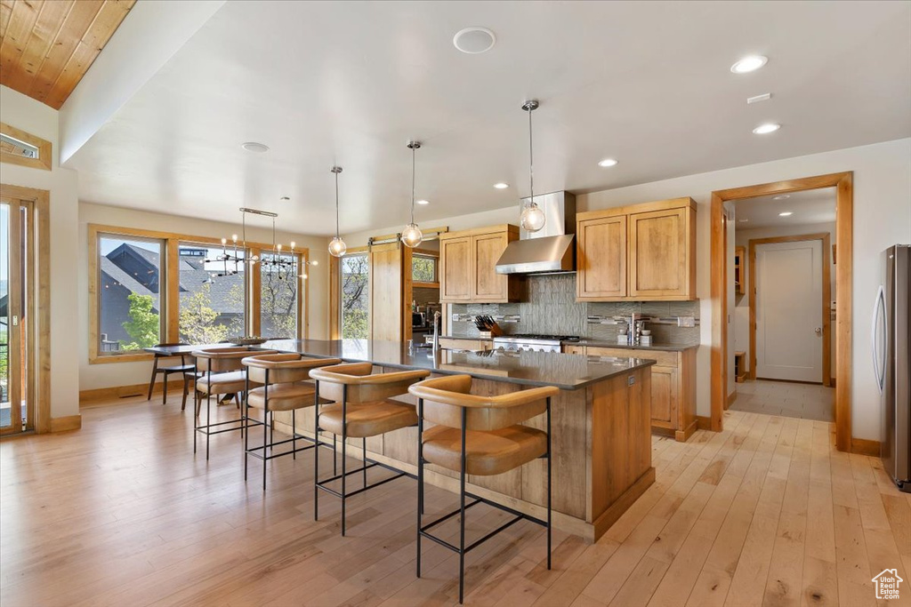 Kitchen featuring wall chimney exhaust hood, light wood-style flooring, a spacious island, tasteful backsplash, and recessed lighting