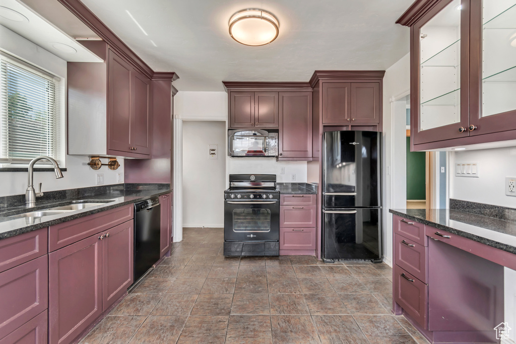 Kitchen featuring black appliances, a sink, glass insert cabinets, dark stone counters, and stone finish floors