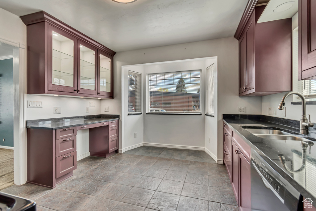 Kitchen featuring a sink, dishwasher, baseboards, dark stone countertops, and light stone finish flooring