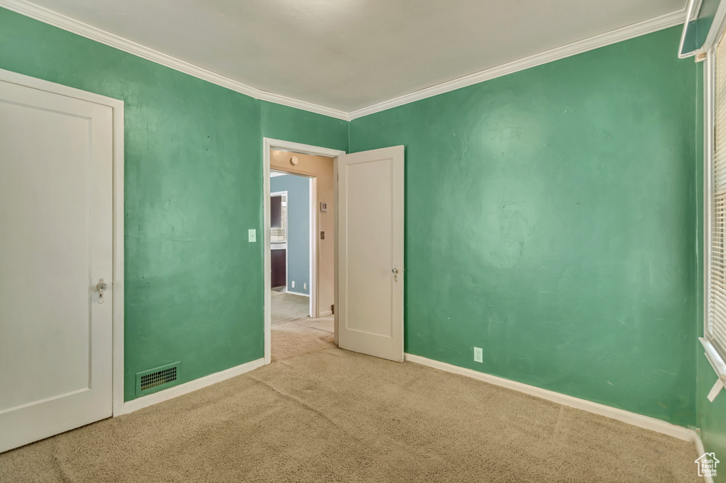 Carpeted spare room featuring crown molding and baseboards