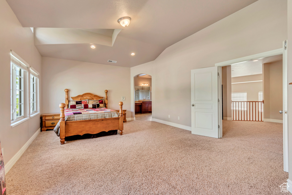 Bedroom featuring lofted ceiling, arched walkways, light colored carpet, baseboards, and recessed lighting