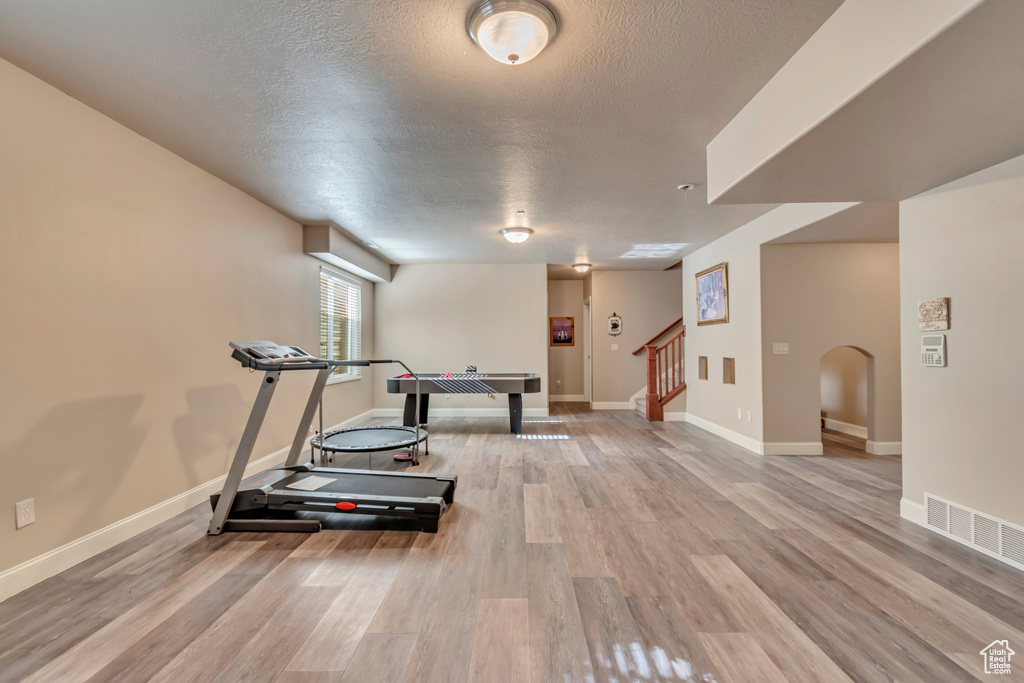 Exercise area featuring wood finished floors, a textured ceiling, baseboards, and arched walkways