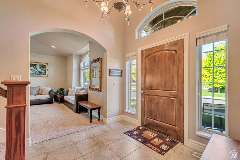Foyer featuring arched walkways, light tile patterned floors, light carpet, baseboards, and a chandelier