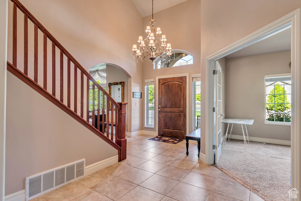 Foyer entrance featuring baseboards, arched walkways, light tile patterned flooring, high vaulted ceiling, and stairs