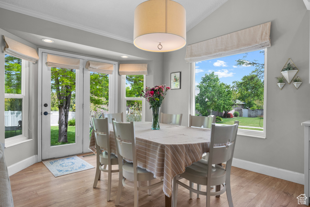 Dining room with baseboards, light wood-style flooring, crown molding, and lofted ceiling