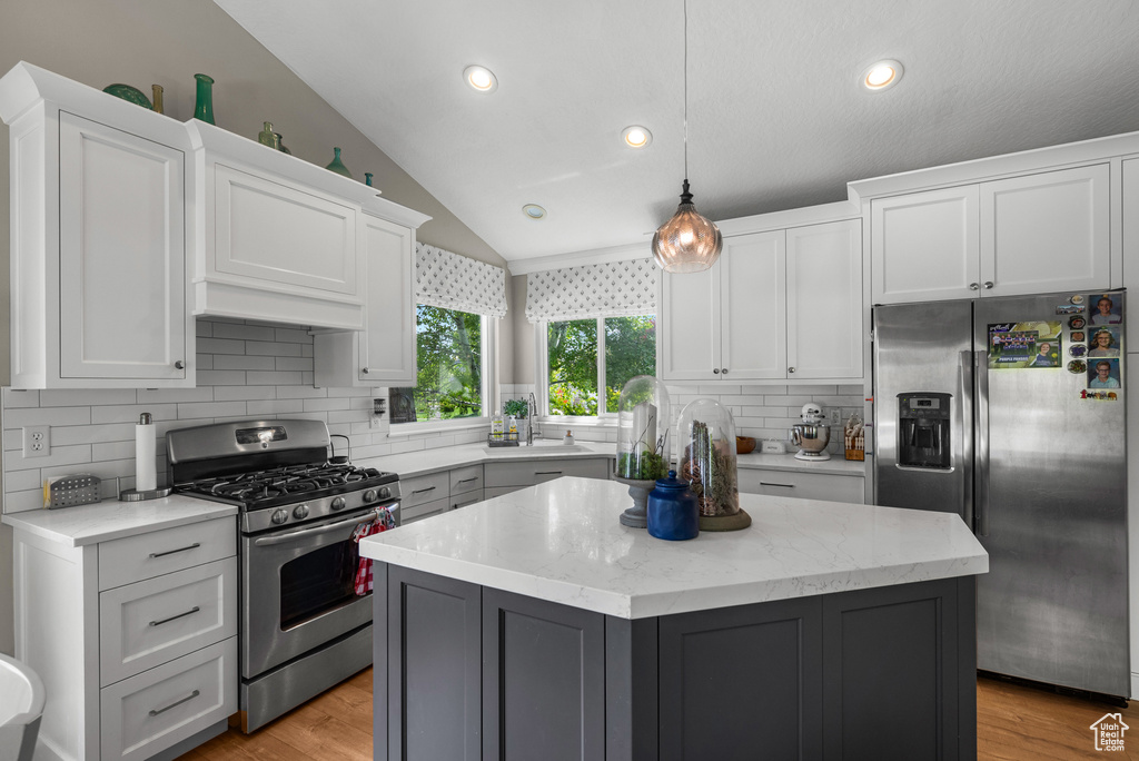 Kitchen with stainless steel appliances, vaulted ceiling, tasteful backsplash, white cabinetry, and a kitchen island