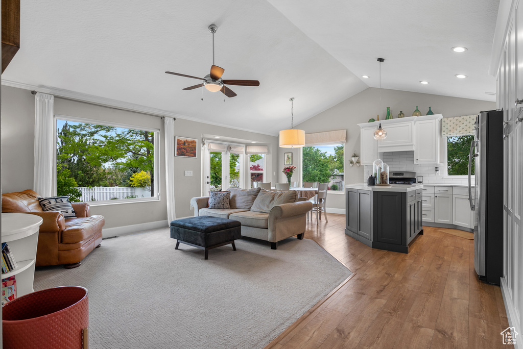 Living area with lofted ceiling, ceiling fan, plenty of natural light, light wood-style flooring, and baseboards