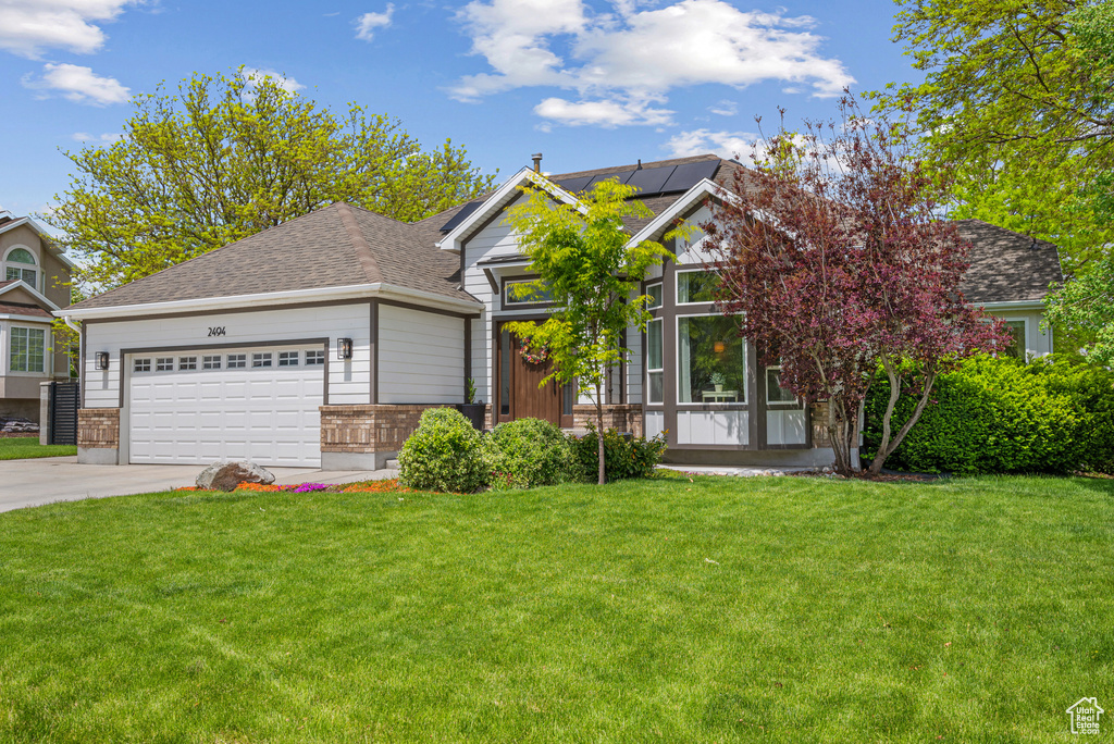 View of front of property with driveway, a garage, roof mounted solar panels, a front lawn, and brick siding
