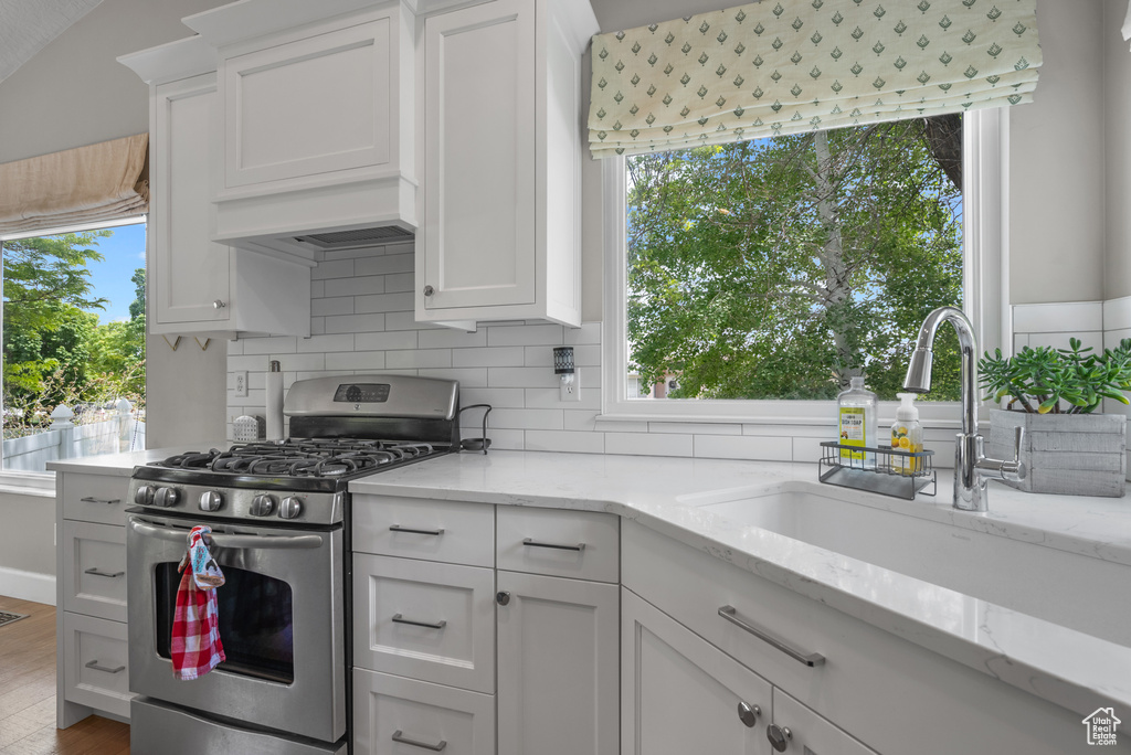 Kitchen featuring stainless steel gas range oven, a sink, white cabinets, and tasteful backsplash