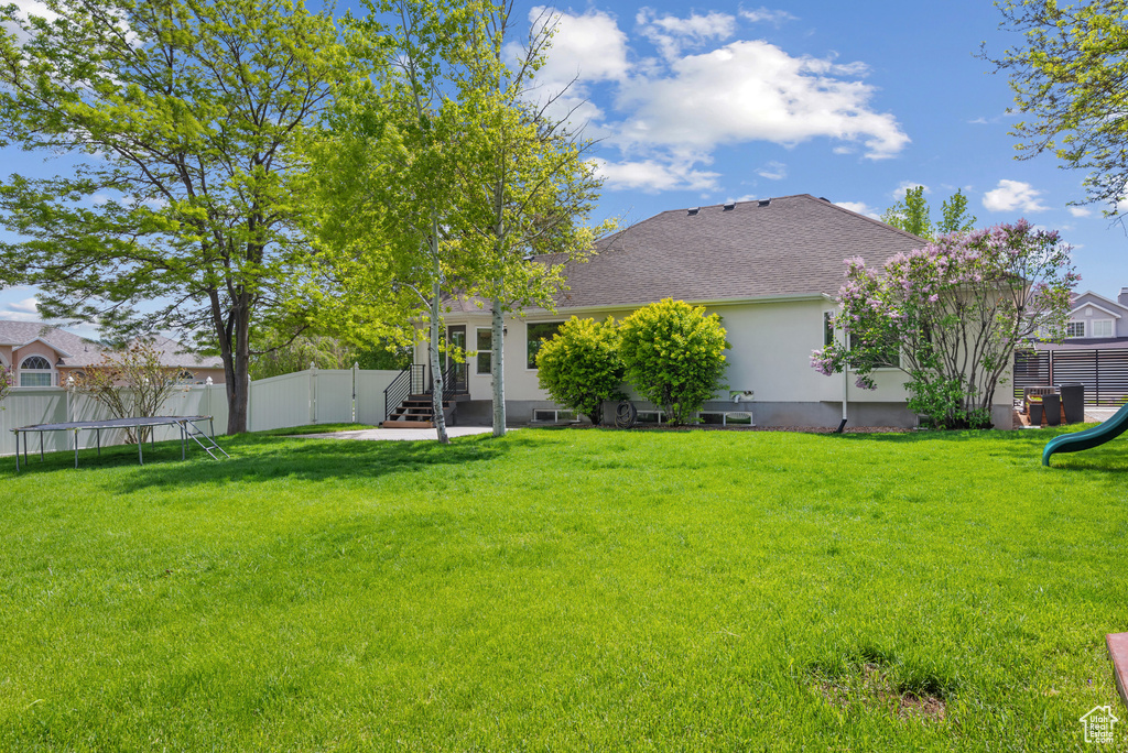 Rear view of house featuring a trampoline, a playground, stucco siding, roof with shingles, and entry steps