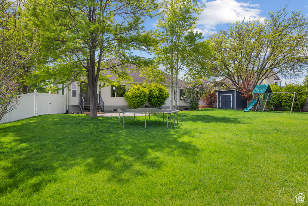 View of yard featuring a playground, a shed, entry steps, a trampoline, and an outbuilding