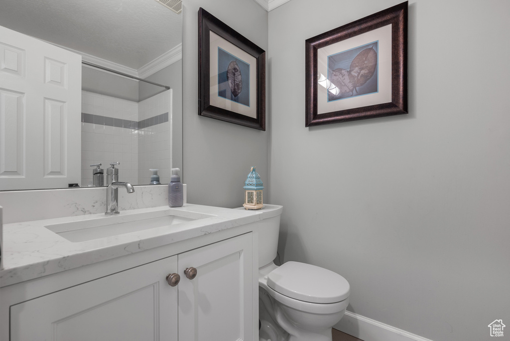 Full bathroom with toilet, ornamental molding, tiled shower, and vanity