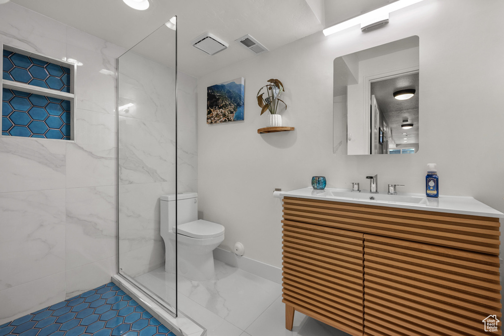Bathroom with toilet, a marble finish shower, and vanity