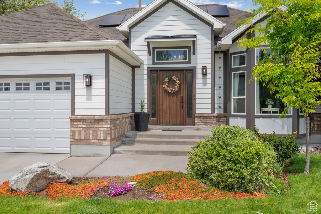 Property entrance with brick siding, roof mounted solar panels, and roof with shingles