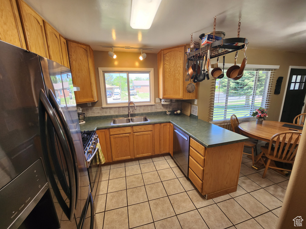 Kitchen featuring stainless steel appliances, a sink, a peninsula, rail lighting, and dark countertops