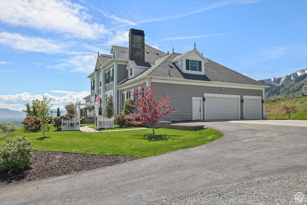 View of front facade with asphalt driveway, a chimney, a garage, and a mountain view