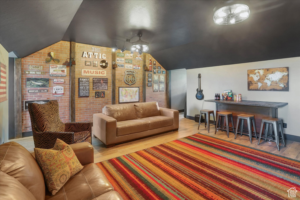 Living room featuring vaulted ceiling, baseboards, brick wall, and wood finished floors