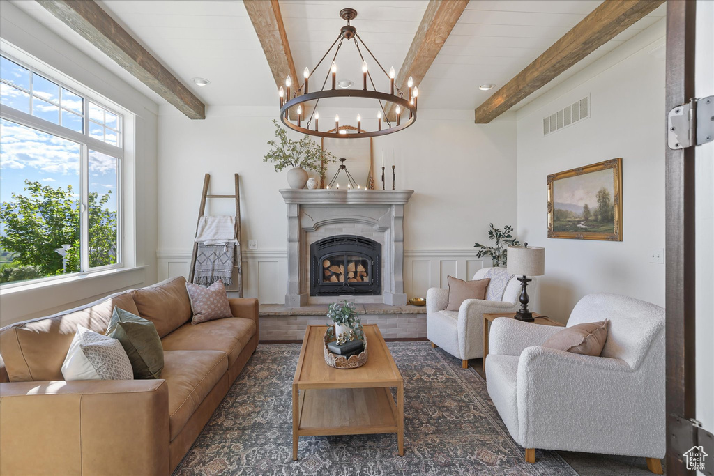 Living area featuring beam ceiling, a chandelier, a fireplace with raised hearth, a decorative wall, and wainscoting