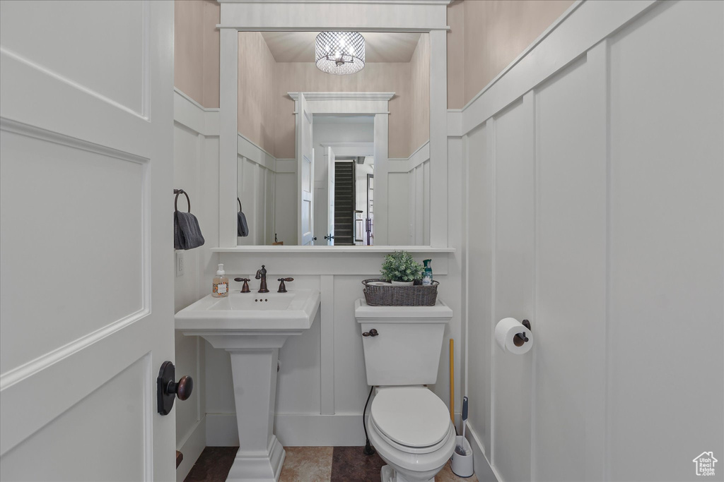 Half bathroom with a decorative wall, toilet, and wainscoting