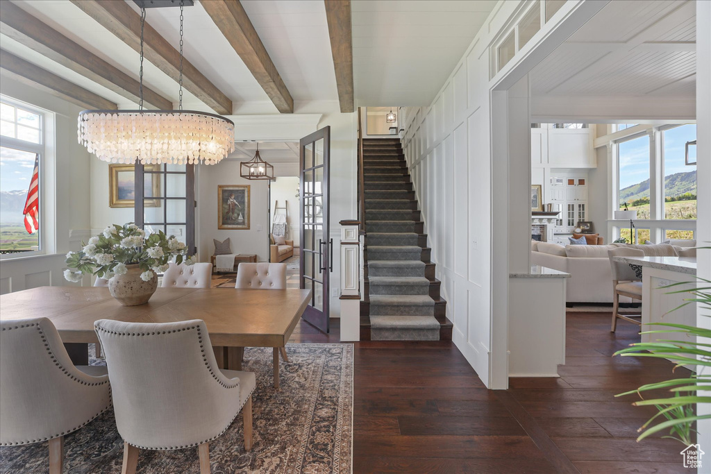 Dining area featuring stairway, dark wood-style flooring, healthy amount of natural light, a chandelier, and beamed ceiling
