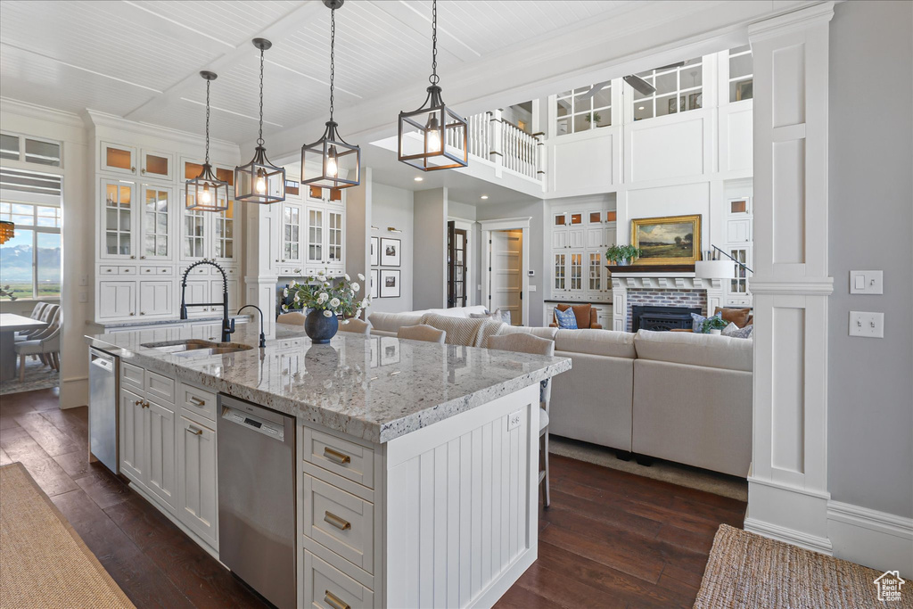 Kitchen with dishwasher, a sink, dark wood-type flooring, an island with sink, and glass insert cabinets
