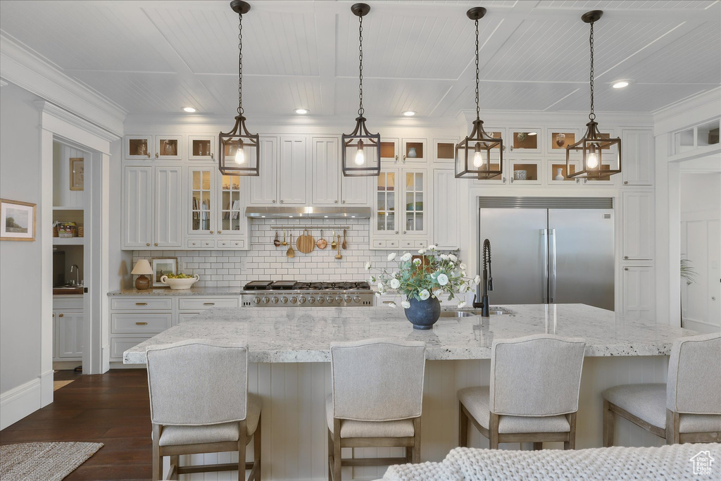 Kitchen with stainless steel built in fridge, a sink, white cabinets, dark wood-style flooring, and decorative backsplash