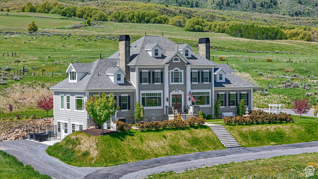 View of front facade featuring a chimney, a front yard, a shingled roof, and a rural view