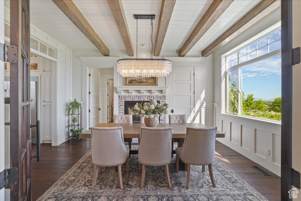 Dining area featuring beamed ceiling, dark wood-type flooring, a decorative wall, and a chandelier
