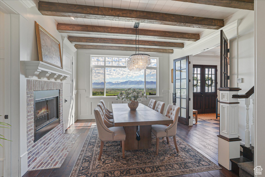 Dining space with dark wood-style flooring, a brick fireplace, french doors, a chandelier, and beamed ceiling
