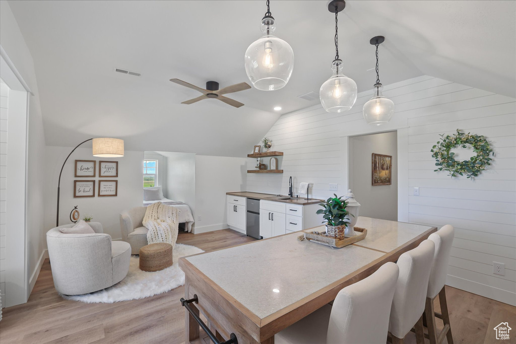 Dining room featuring vaulted ceiling, light wood-type flooring, baseboards, a ceiling fan, and wooden walls