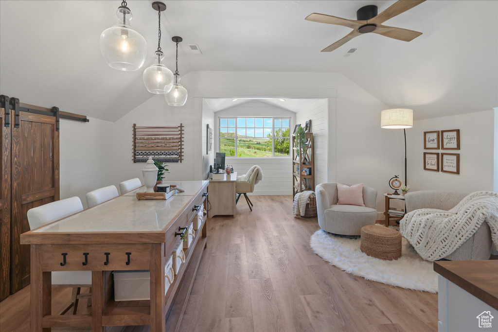 Home office with a barn door, vaulted ceiling, a ceiling fan, and light wood-style flooring