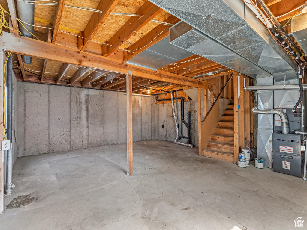 Unfinished below grade area featuring heating unit and stairs
