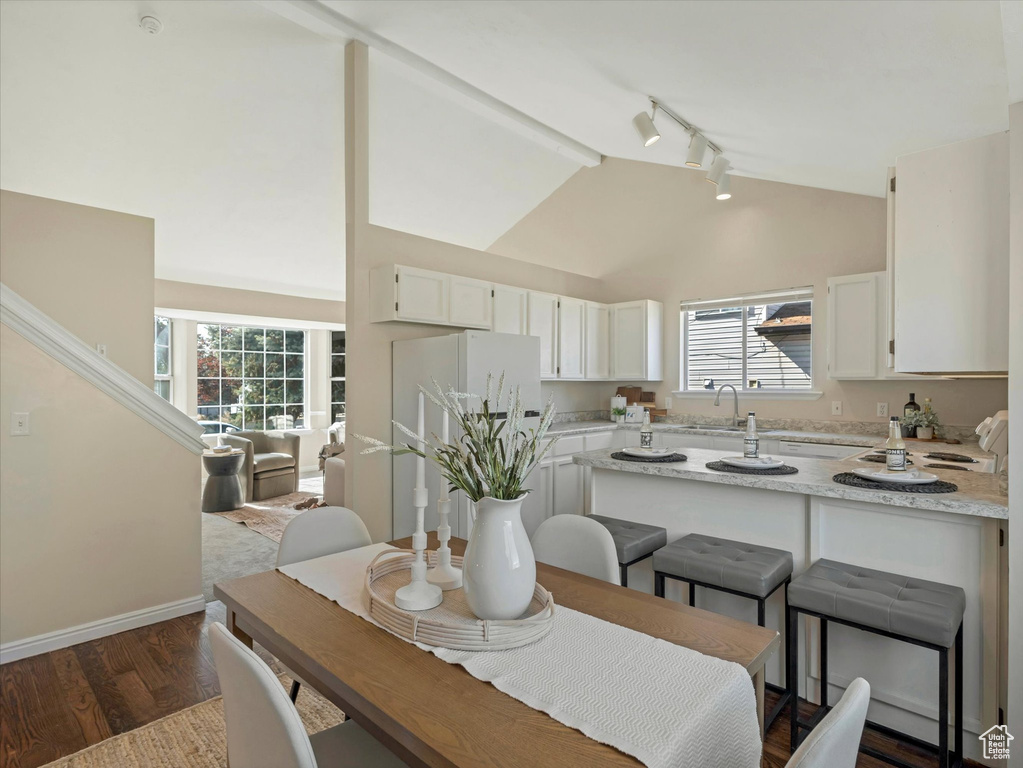 Dining space with rail lighting, dark wood-style flooring, baseboards, and high vaulted ceiling