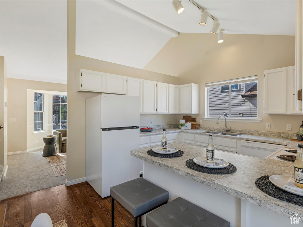 Kitchen with white appliances, a sink, track lighting, dark wood finished floors, and white cabinets