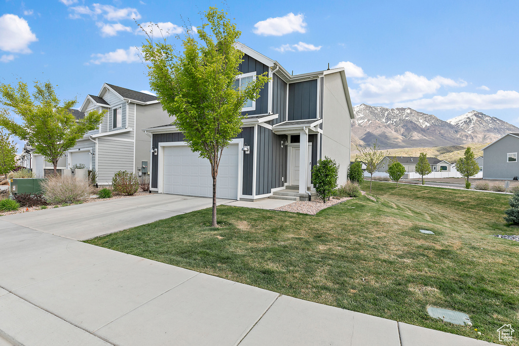 Traditional-style house featuring board and batten siding, concrete driveway, a mountain view, and a front lawn