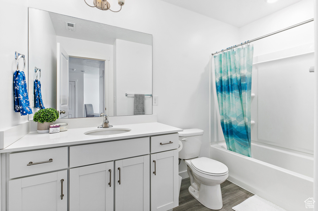 Bathroom with toilet, wood finished floors, vanity, and shower / tub combo