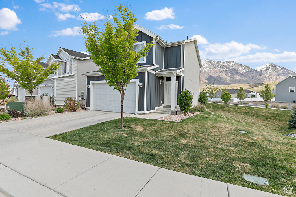 Traditional home with board and batten siding, driveway, a mountain view, and a front lawn
