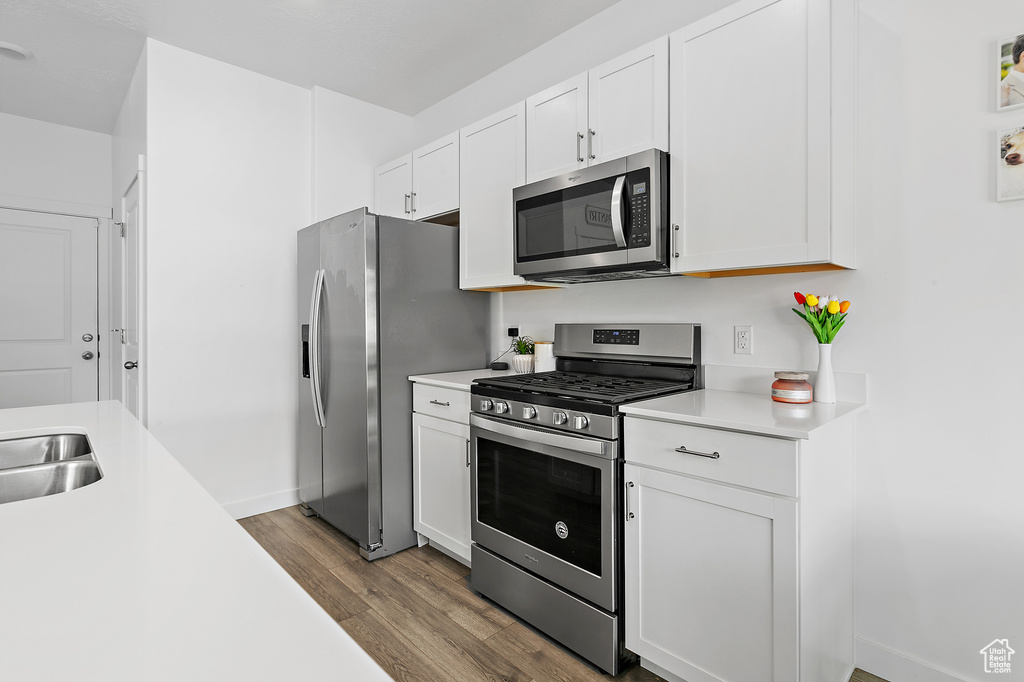 Kitchen featuring appliances with stainless steel finishes, wood finished floors, light countertops, white cabinetry, and baseboards