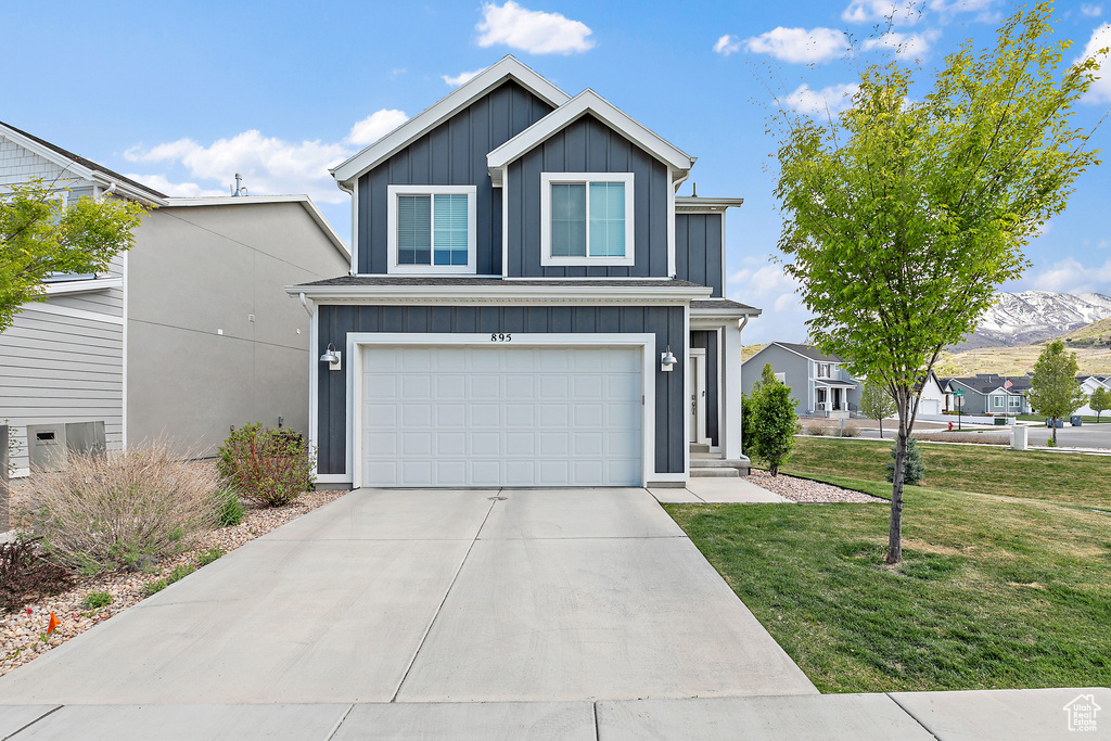 Traditional home featuring board and batten siding, a front yard, a garage, concrete driveway, and a mountain view