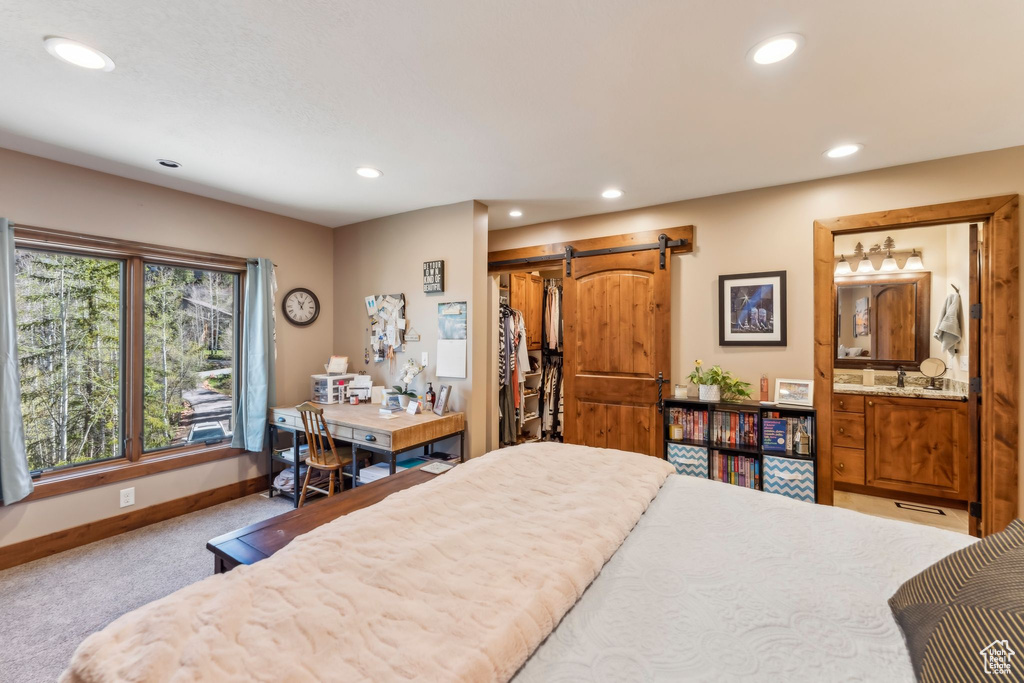 Bedroom with a barn door, recessed lighting, carpet flooring, baseboards, and ensuite bathroom
