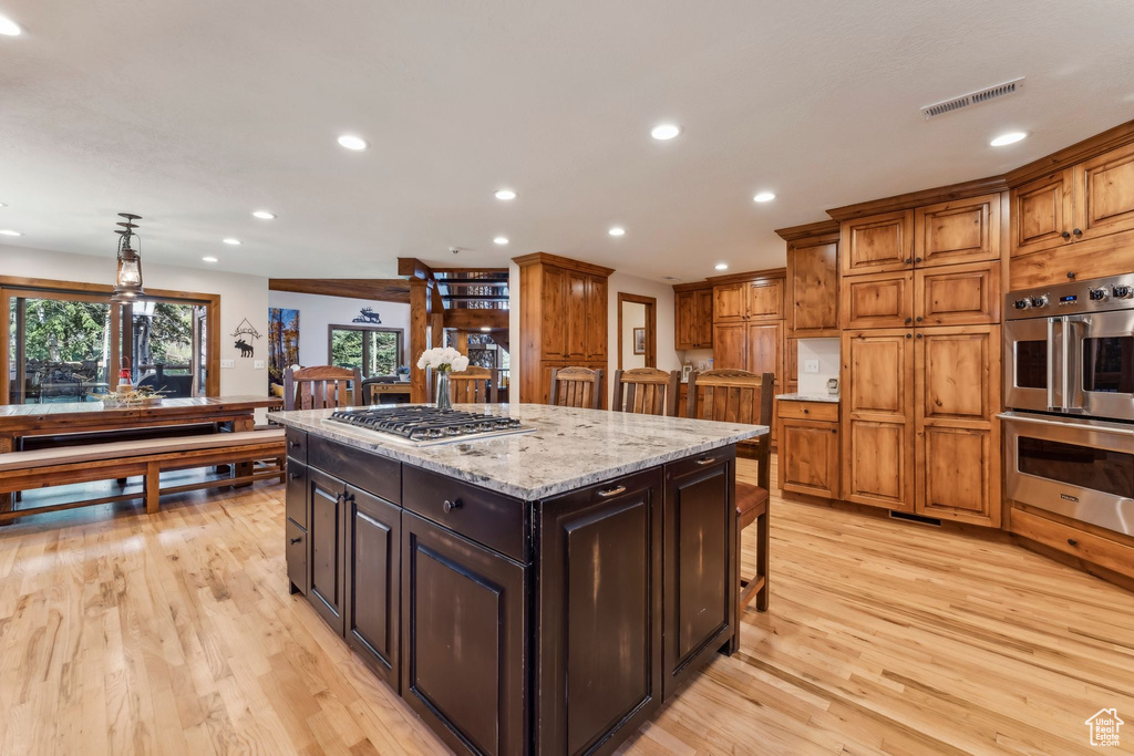 Kitchen featuring stainless steel appliances, a kitchen island, light wood finished floors, recessed lighting, and a breakfast bar