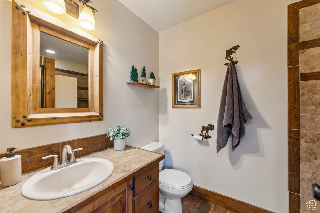 Full bath with toilet, vanity, wood finished floors, and tiled shower