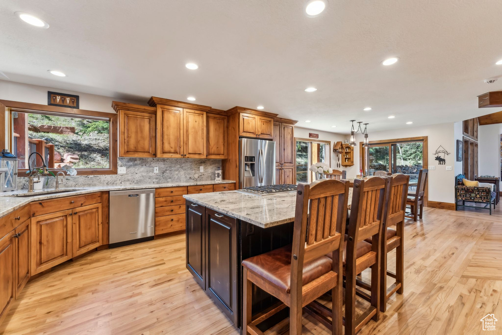 Kitchen with appliances with stainless steel finishes, recessed lighting, a sink, brown cabinets, and a kitchen bar