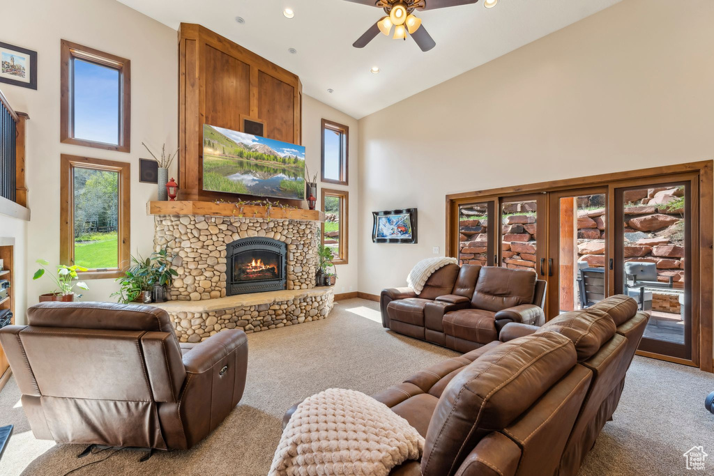 Living room featuring a stone fireplace, carpet flooring, high vaulted ceiling, a ceiling fan, and baseboards