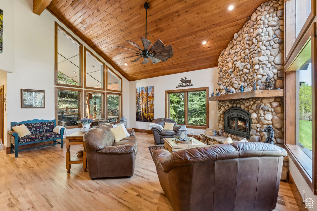 Living room with wood ceiling, high vaulted ceiling, a stone fireplace, ceiling fan, and light wood-style flooring
