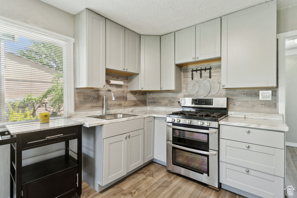 Kitchen with range with two ovens, a sink, backsplash, light wood-type flooring, and a textured ceiling