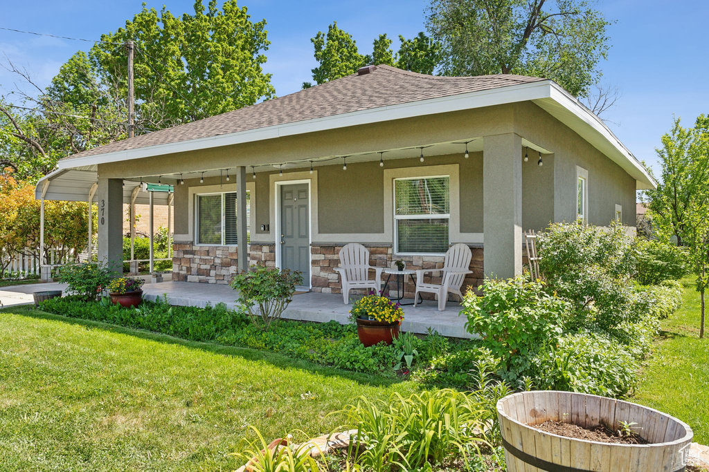 Rear view of house featuring roof with shingles, a yard, stucco siding, and stone siding
