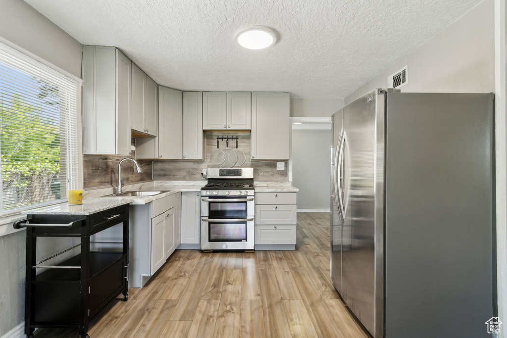 Kitchen with stainless steel appliances, a sink, gray cabinets, light wood-style flooring, and backsplash