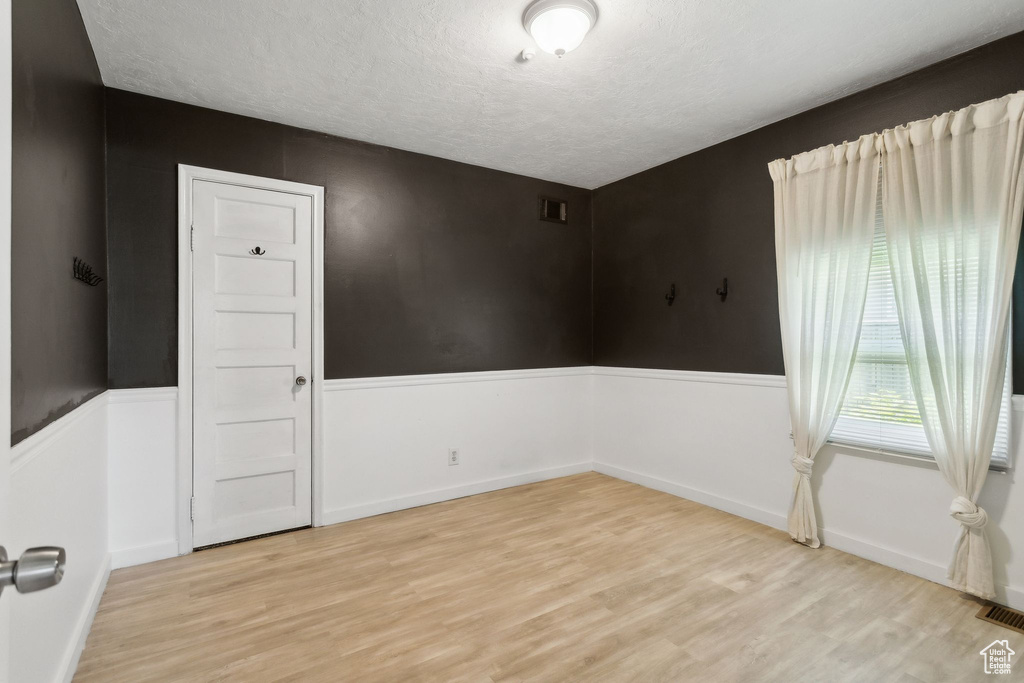 Unfurnished room with light wood finished floors, a textured ceiling, and baseboards