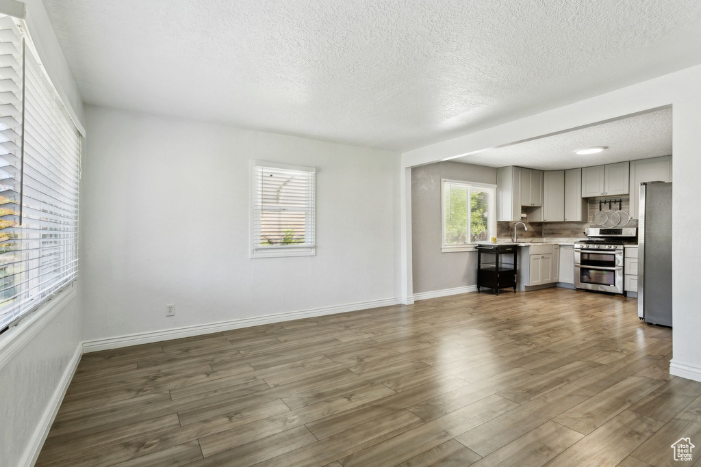 Unfurnished living room with a textured ceiling, a sink, baseboards, and dark wood-type flooring